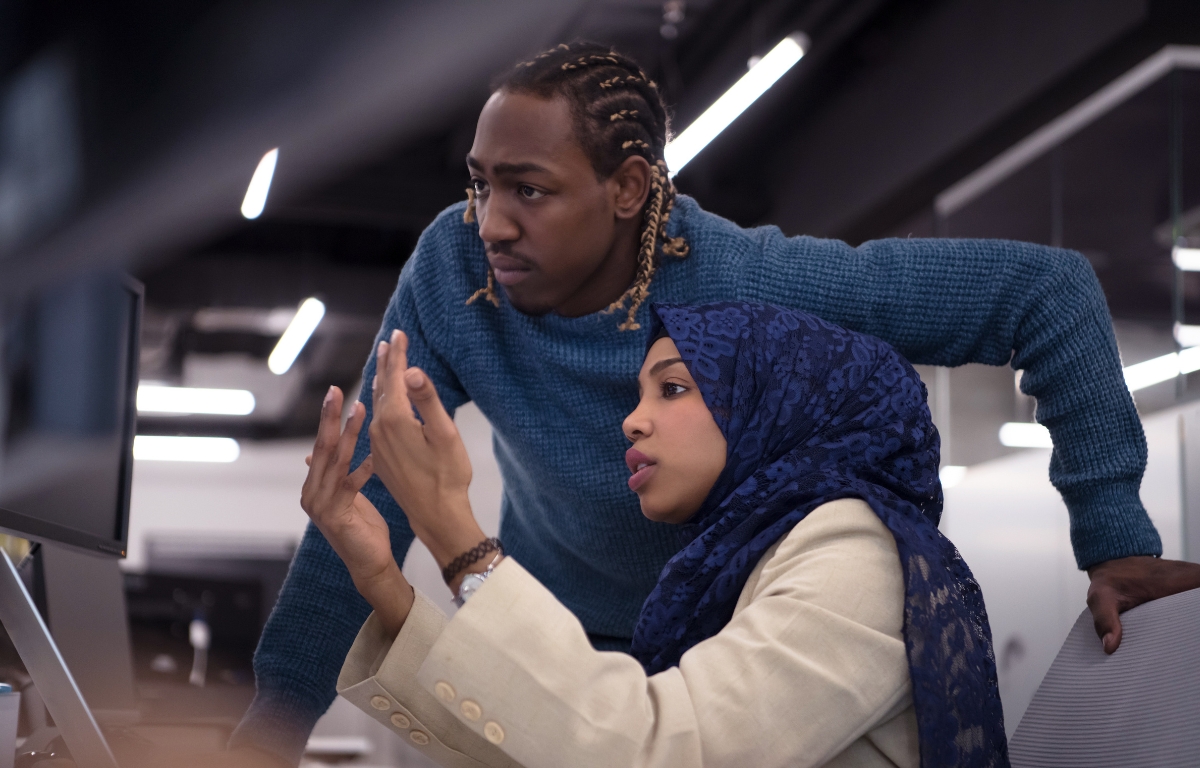 Two people in an office setting look intently at a computer screen. The woman, wearing a hijab, gestures with her hand, while the man leans forward with his hand on his hip. Designed by Circular Design, a not-for-profit web design agency.