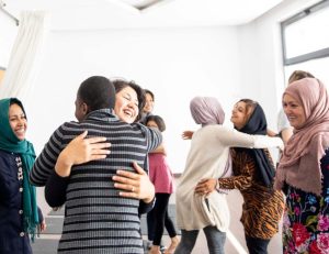 A group of people in a bright room are embracing and smiling at each other, creating a warm and welcoming atmosphere.