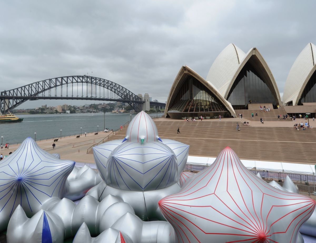 Large silver inflatable structures with red and blue lines are displayed in front of the Sydney Opera House, with the Sydney Harbour Bridge visible in the background under cloudy skies. Designed by Circular Design, a not-for-profit web design agency.